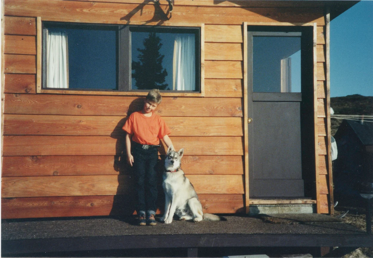 Young boy posing posing in front of house with his husky
