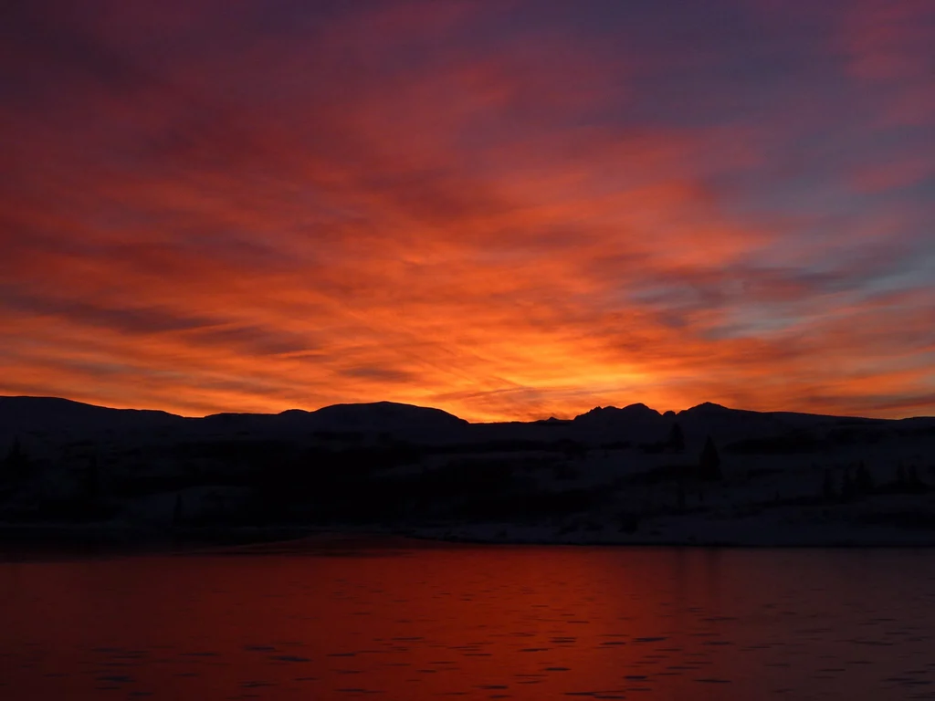 Sunset with mountains and body of water in foreground.