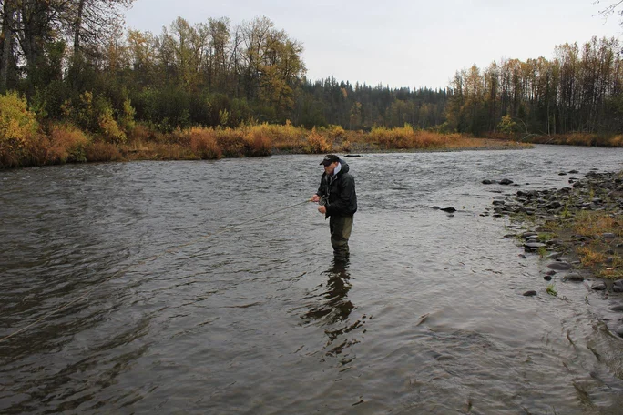 Man holding fishing pole standing in shallow part of river.