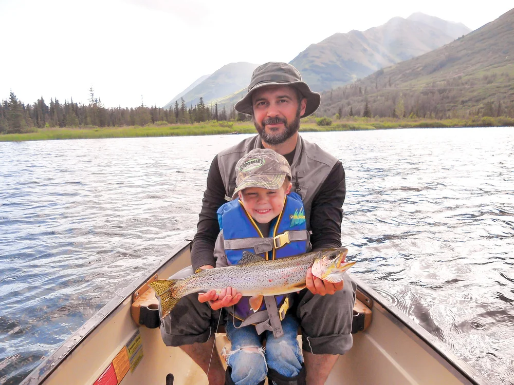 Father and son sitting in a canoe, displaying their caught rainbow trout