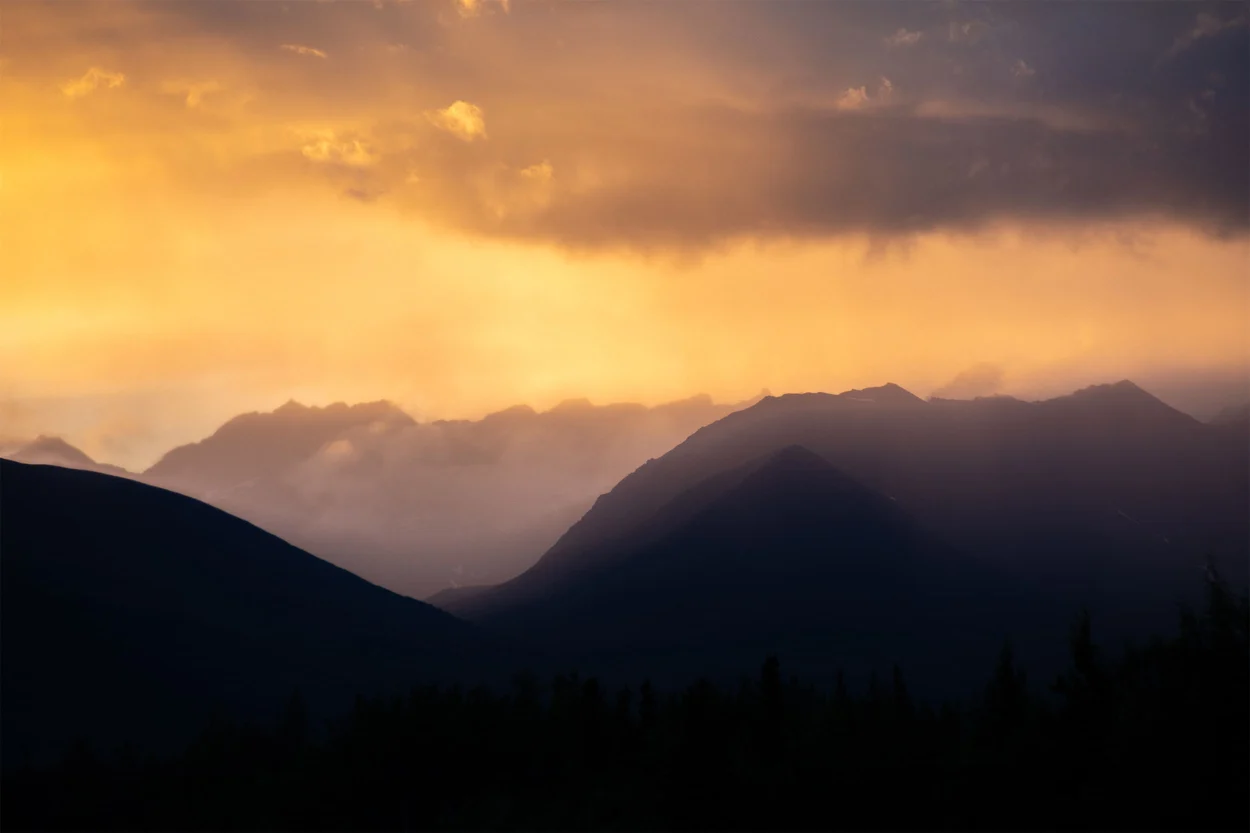 Hazy mountain peaks and golden clouds during sunset.